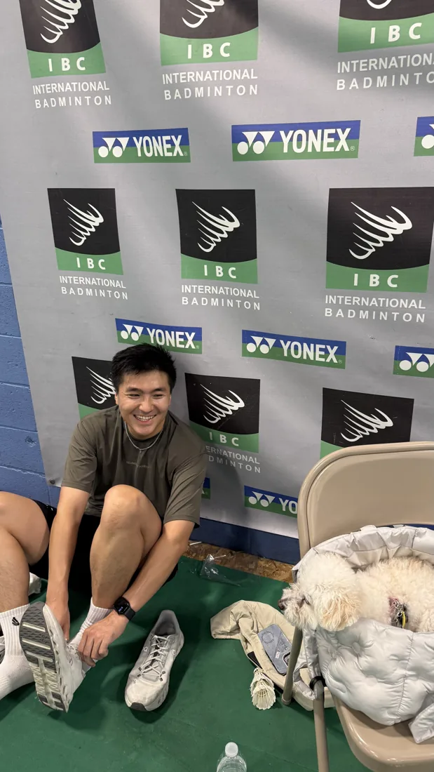 Kelvin sitting courtside at an international badminton tournament with his gear
