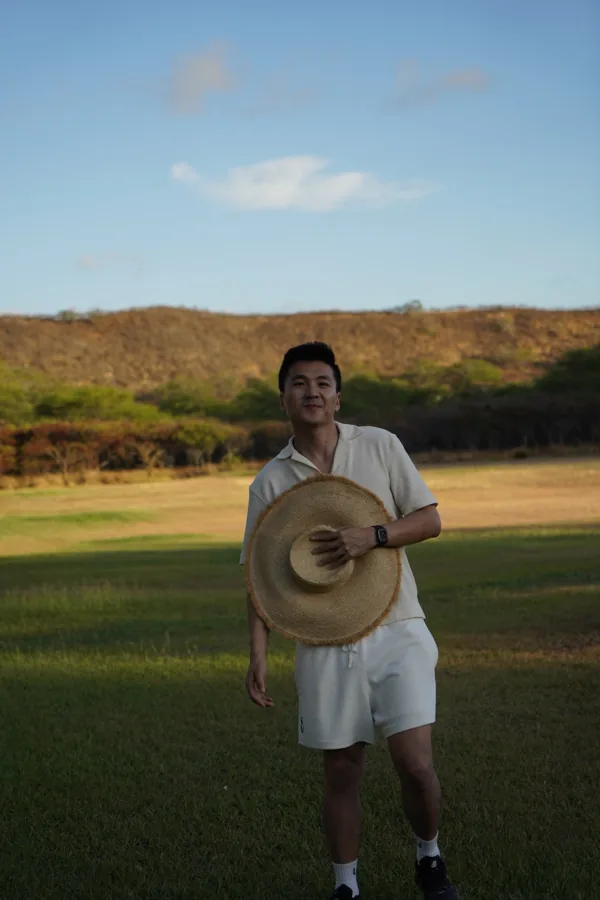 Kelvin standing in a golden field at sunset holding a hat