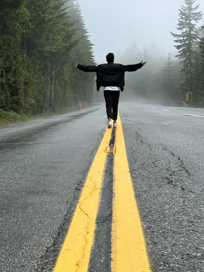 Kelvin jumping with both arms raised on the yellow centerline of an empty foggy road